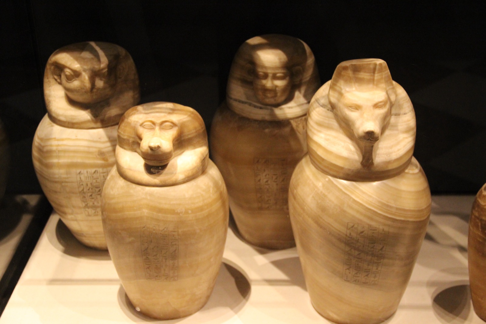 Four ancient Egyptian alabaster canopic jars with carved lids representing the Four Sons of Horus
