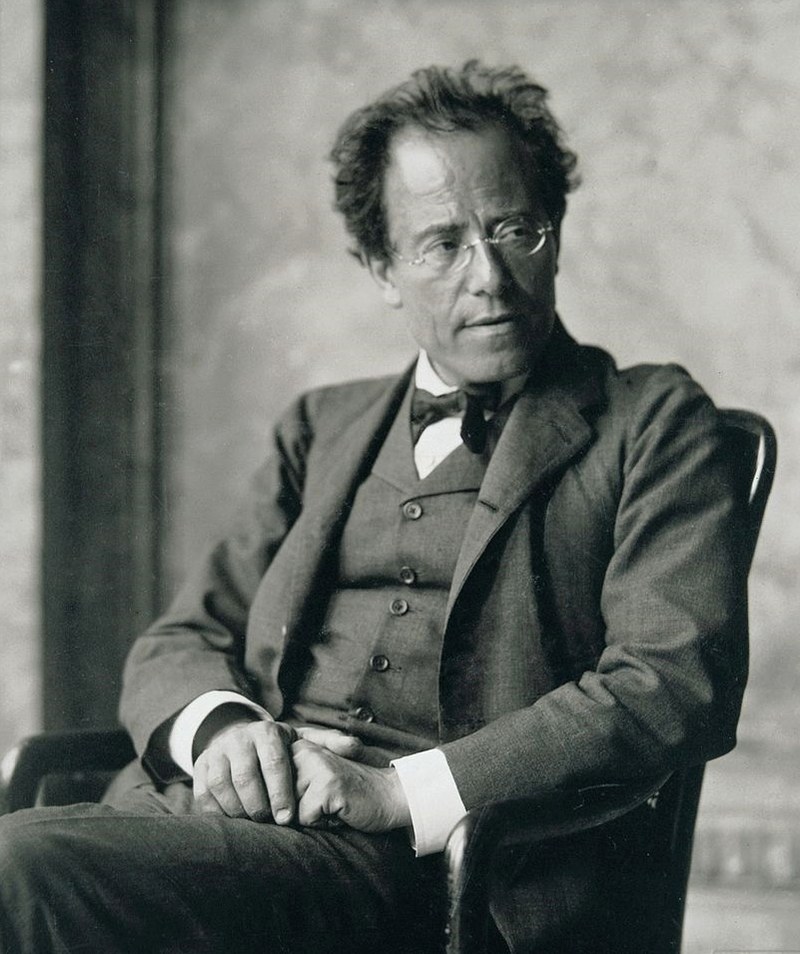 Photograph of composer Gustav Mahler seated, wearing round wire glasses and a dark suit