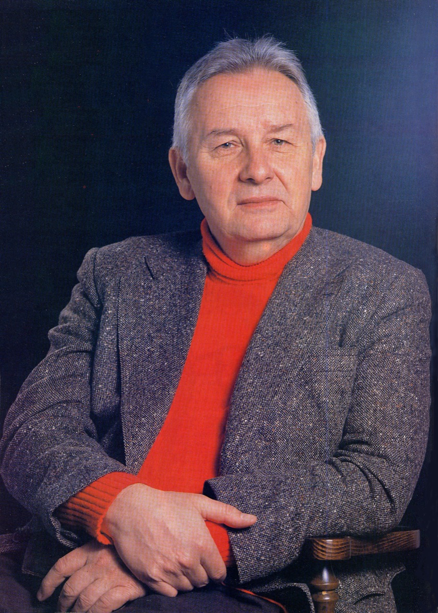 Portrait photograph of Polish composer Henryk Mikolaj Gorecki, an older man with white hair in a grey jacket and red turtleneck