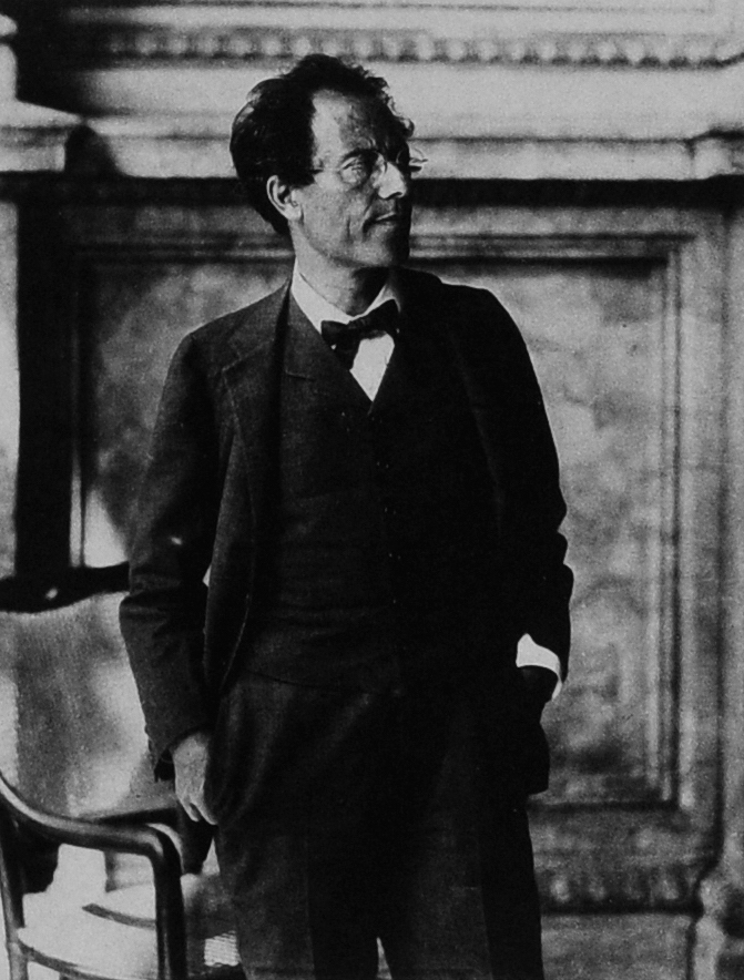 Black and white photograph of composer Gustav Mahler standing indoors wearing round spectacles