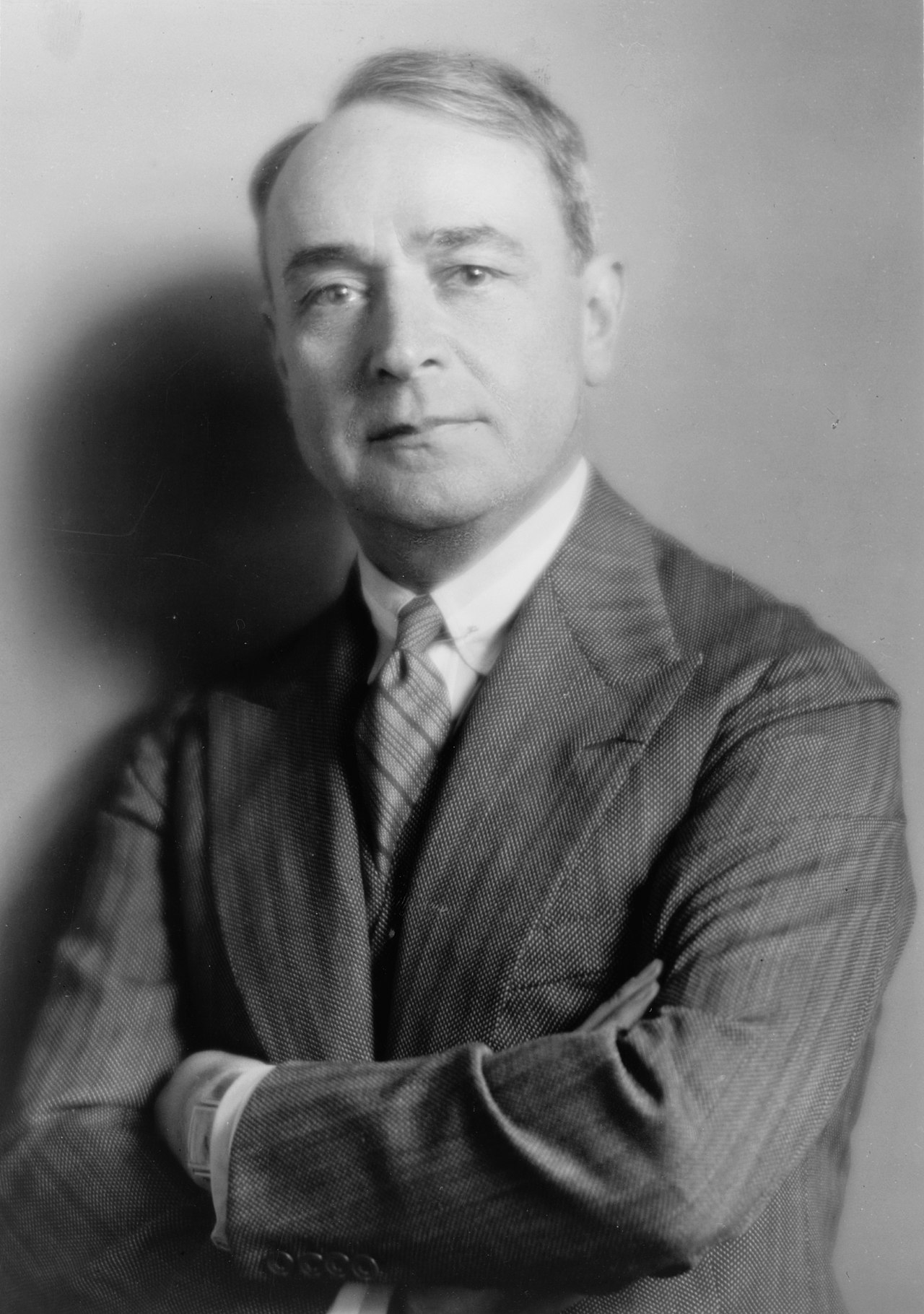 Black-and-white studio portrait of the conductor Serge Koussevitzky standing with his arms folded
