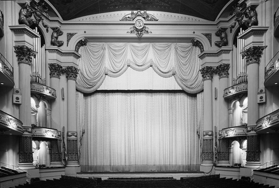 The ornate gilded proscenium arch and closed stage curtain of the Academy of Music in Philadelphia